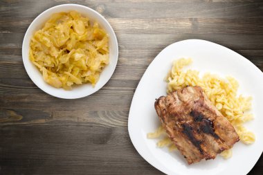 Izgara domuz pirzolası ve makarna. Beyaz tabakta ızgara domuz kaburgası ve siyah ahşap arka plan. Izgara domuz pirzolası.