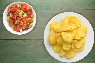 Beyaz tabakta patates cipsi ve vejetaryen salatası. yeşil ahşap arkaplan görünümlü çipler.