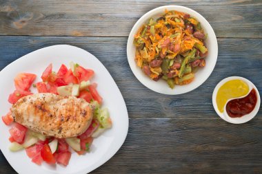 Domates salatası, salatalık ve soğanlı ızgara tavuk göğsü. Mavi ahşap arka planda beyaz tabakta ızgara tavuk göğsü. Kızarmış tavuk göğsü manzaralı. Düz yatıyordu.