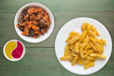 Yeşil ahşap arka planda beyaz bir tabakta patates kızartması. Sebze salatalı patates kızartması. Sağlıksız yiyecekler