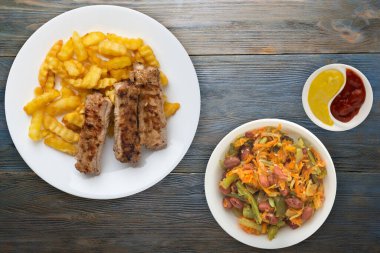 Beyaz bir tabakta domuz pirzolası ve patates ve sebze salatası ve gri mavi ahşap arka planda sos. Fast food 'un en iyi manzarası. Sağlıksız yiyecekler.