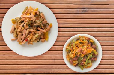 Turuncu ahşap arka planda beyaz bir tabakta Berlin salatası. Sosis, salatalık, biber soslu salata. .