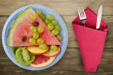 Kahverengi ahşap arka planda çatal ve bıçakla dilimlenmiş meyve. Açık mavi bir tabakta dilimlenmiş meyve manzarası