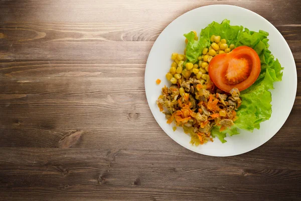 salad with chicken stomachs with carrots and corn and salad on a white plate. chicken salad with vegetables on a brown wooden background
