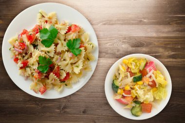 Beyaz tabakta makarna. Makarna, domates, soğan, kahverengi ahşap arka planda lahana. Vejetaryen salata soslu makarna.