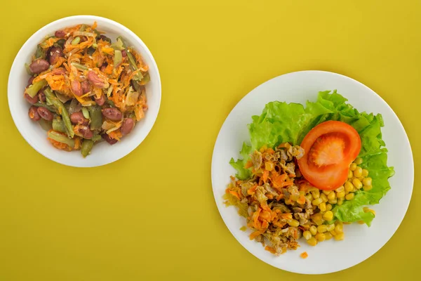 salad with chicken stomachs with carrots and corn and salad on a white plate. chicken salad with vegetables on a yellow background