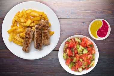 Beyaz tabakta domuz pirzolası ve patates, sebze salatası ve mor ahşap arka planda sos. Fast food 'un en iyi manzarası. Sağlıksız yiyecekler.