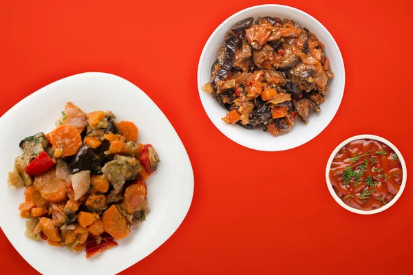 vegetable stew on a white plate. stewed vegetables on a red background. vegetarian food.flat lay