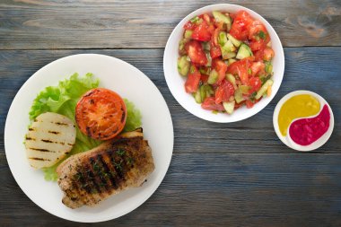  Mavi ahşap arka planda patates ve domatesle ızgara domuz eti. Salata soslu ızgara domuz eti.
