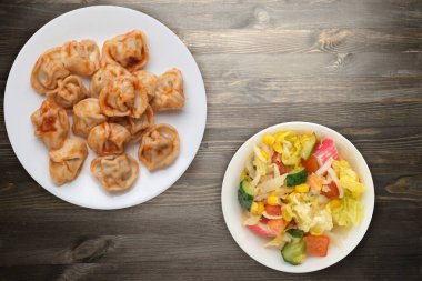 Siyah ahşap arka planda beyaz tabakta hamur tatlısı. Salatalı domates soslu börek. Hamur köftesi üst görünüm