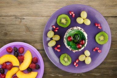 Kek ve meyve üzümleri, kivi, ahşap zemin üzerinde nar. Mor bir tabakta meyveli tatlı.