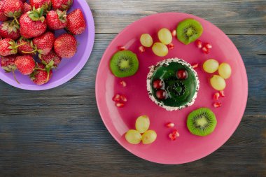 Kek ve meyve üzümleri, kivi, mavi ahşap zemin üzerinde nar. Tatlı pembe bir tabakta.