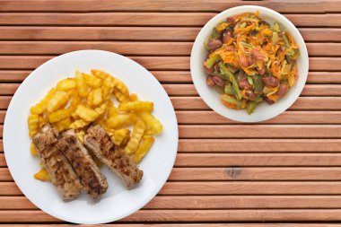 Beyaz tabakta domuz pirzolası ve patates, sebze salatası ve portakal ağacından arkaplanda sos. Fast food 'un en iyi manzarası. Sağlıksız yiyecekler.