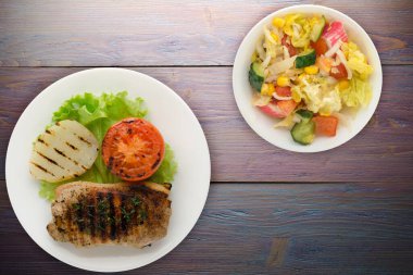 Mor ahşap arka planda patates ve domatesle ızgara domuz eti. Salata soslu ızgara domuz eti.