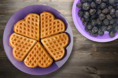 Siyah ahşap arka planda meyveli Belçika waffle 'ları. Mor bir tabakta waffle.