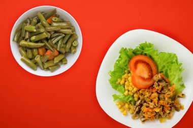salad with chicken stomachs with carrots and corn and salad on a white plate. chicken salad with vegetables on a red background