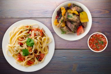 Vejetaryen salata manzaralı beyaz tabakta spagetti. domatesler, soğanlar, lahanalar mor ahşap arka planda.