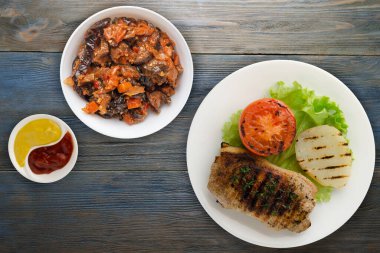 Mavi ahşap arka planda patates ve domatesle ızgara domuz eti. Salata soslu ızgara domuz eti.