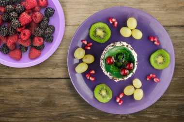 Kek ve meyve üzümleri, kivi, ahşap zemin üzerinde nar. Mor bir tabakta meyveli tatlı.