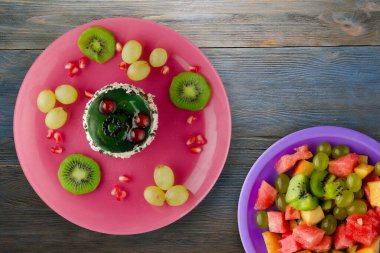 Kek ve meyve üzümleri, kivi, mavi ahşap zemin üzerinde nar. Tatlı pembe bir tabakta.