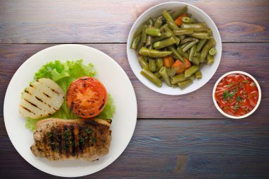  Mor ahşap arka planda patates ve domatesle ızgara domuz eti. Salata soslu ızgara domuz eti.