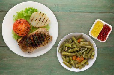  Yeşil ahşap zemin üzerinde patates ve domatesle ızgara domuz eti. Salata soslu ızgara domuz eti.