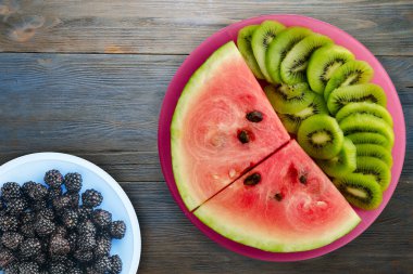 Kırmızı bir tabakta karpuz ve kivi dilimlenmiş mavi gri ahşap arka plan manzaralı meyve salatası.