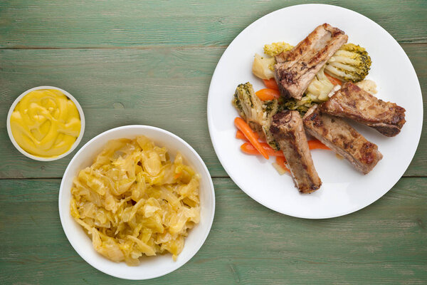 grilled pork ribs with broccoli cabbage, carrots and garlic on a white  plate. fried pork ribs with vegetables on a green wooden background. hearty rustic food top view