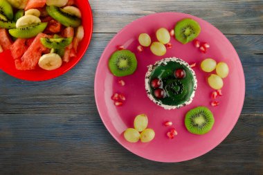 Kek ve meyve üzümleri, kivi, mavi ahşap zemin üzerinde nar. Tatlı pembe bir tabakta.