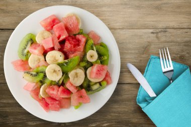 Kahverengi ahşap zemin üzerinde sağlıklı taze meyve salatası. Çatallı ve diz kapaklı meyve salatası.