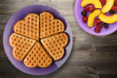 Siyah ahşap arka planda meyveli Belçika waffle 'ları. Mor bir tabakta waffle.