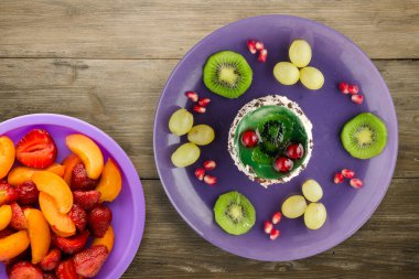 Kek ve meyve üzümleri, kivi, ahşap zemin üzerinde nar. Mor bir tabakta meyveli tatlı.