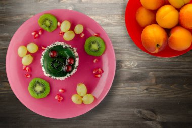 Kek ve meyve üzümleri, kivi, siyah ahşap zemin üzerinde nar. Pembe tabakta meyveli tatlı.