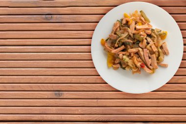 Turuncu ahşap arka planda beyaz bir tabakta Berlin salatası. Sosis, salatalık, biber soslu salata. .