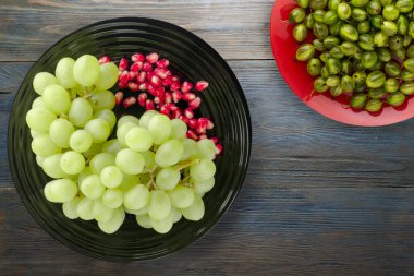 Üzüm, mavi ahşap arka planda nar. Üzüm, nar, siyah bir tabakta üst manzara.