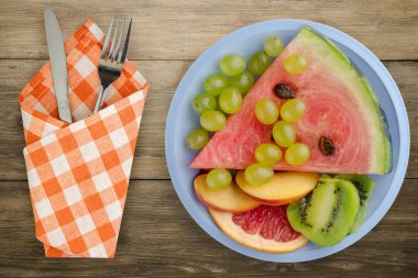 Ahşap bir arka planda dilimlenmiş meyve. Dilimlenmiş meyve, açık mavi bir tabakta üst görünümde. Dilimlenmiş meyve, çatal ve bıçak.