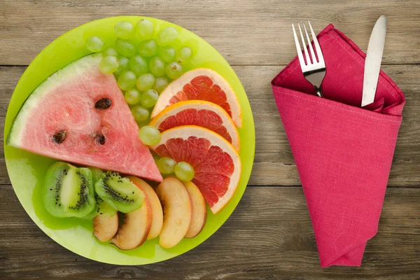 sliced fruit on a borwn wooden background. sliced fruit on a light green plate fork and knife top view