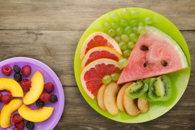 Doğuştan ahşap arka planda kesilmiş meyve. Açık yeşil bir tabakta dilimlenmiş meyve ince zeka meyveleri mor bir tabakta.