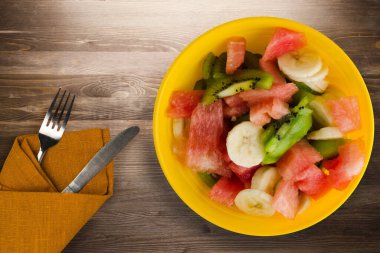Kahverengi ahşap tabakta sağlıklı taze meyve salatası. Çatal ve bıçak üst görüşlü vejetaryen salatası. .