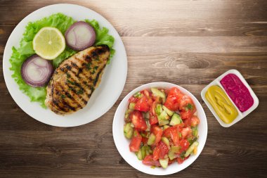 Sebzeli ızgara tavuk fileto limon, salata, kahverengi ahşap arka planda soğan. Tavuklu fileto, beyaz tabak şeklinde ızgara.