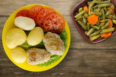 Sarı tabakta patates ve sebze salatası manzaralı pirzola. Kahverengi ahşap arka planda patatesli pirzola