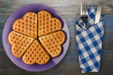 Belçika waffle 'ı mavi ahşap arka plan. Çatal ve bıçak manzaralı mor bir tabakta waffle.