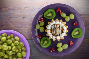 Kek ve meyve üzümleri, kivi, mor ahşap arka planda nar. Mor tabak manzaralı tatlı.