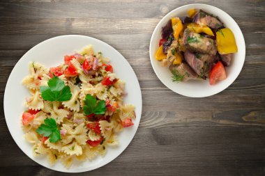 Beyaz tabakta makarna. Makarna, domates, soğan, siyah ahşap arka planda lahana. Vejetaryen salata soslu makarna.