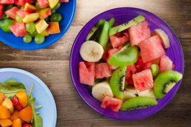 Kahverengi ahşap zemin üzerinde sağlıklı taze meyve salatası. Meyveler en tepede. Vejetaryen yiyecekler.