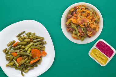   Yeşil arka planda beyaz bir tabakta sarımsaklı havuçlu yeşil fasulye. Vejetaryen salatası ve soslu havuçlu yeşil fasulye. Sağlıklı vejetaryen yemekleri.