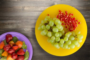 Üzüm, siyah ahşap arka planda nar. Üzüm, nar, sarı bir tabakta.