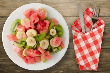 Kahverengi ahşap zemin üzerinde sağlıklı taze meyve salatası. Çatallı ve diz kapaklı meyve salatası.