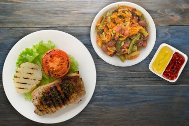 Mavi ahşap arka planda patates ve domatesle ızgara domuz eti. Salata soslu ızgara domuz eti.