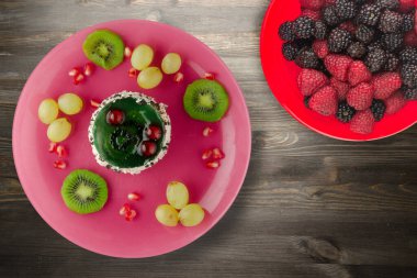 Kek ve meyve üzümleri, kivi, siyah ahşap zemin üzerinde nar. Pembe tabakta meyveli tatlı.